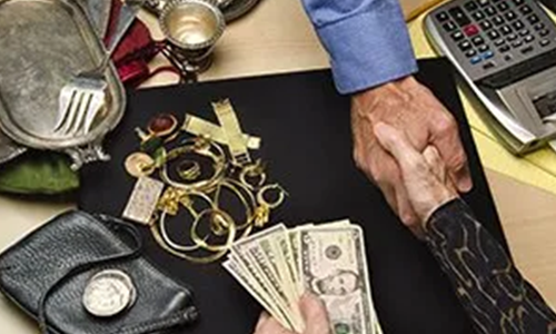 Two individuals shaking hands over a table with assorted items, money, and a calculator. One person holds a stack of cash, and the other has jewelry and small silverware pieces laid out.