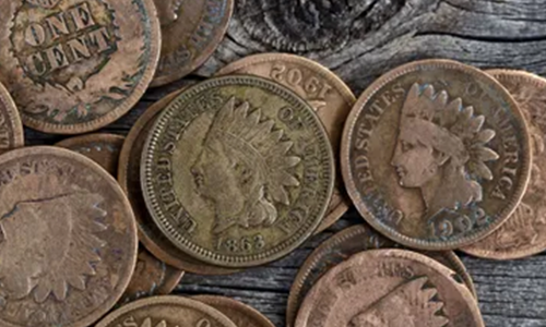 A collection of old, worn United States one-cent coins featuring the Indian Head design, scattered on a wooden surface.